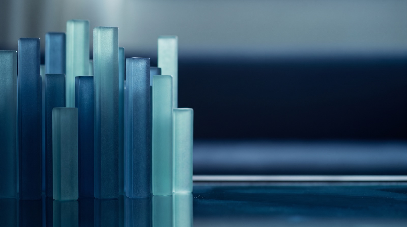 A cluster of frosted blue-green glass columns of uneven height standing on a dark reflective surface