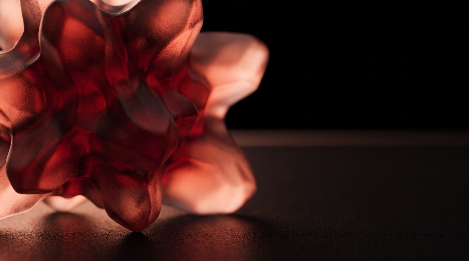 A macro close-up of a translucent red glass form with soft ruffled folds, catching warm light against a black background.